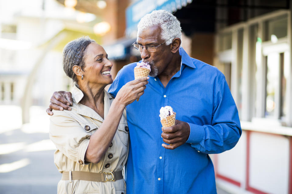 An elderly couple enjoying ice cream cones in the sunshine, smiling and looking happy outside.